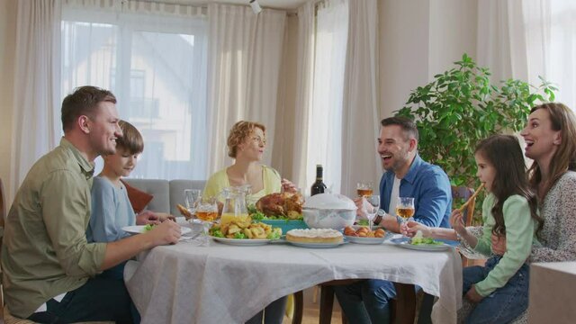 Caucasian people holding glasses with red wine while sitting at dining table, feeling happy and cheery smiling. Party concept
