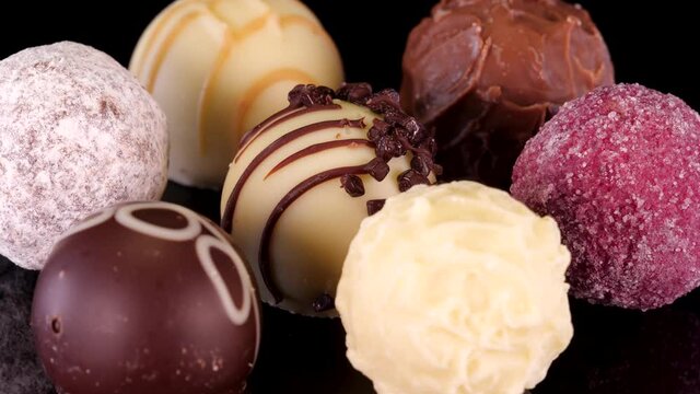 Diverse chocolate pralines and truffles rotating on a black background, close up view. Nicely decorated, premium belgian or swiss chocolate confectionary made with best cocoa. 