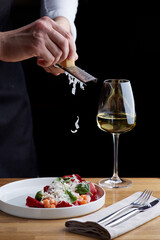 The chef prepares a salad with salmon. Rubs cheese on a grater. salmon salad with beet cheese and green leaves on wooden table with glass of white wine.