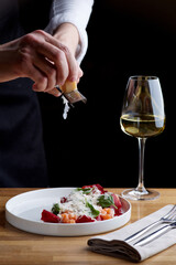 The chef prepares a salad with salmon. Rubs cheese on a grater. salmon salad with beet cheese and green leaves on wooden table with glass of white wine.