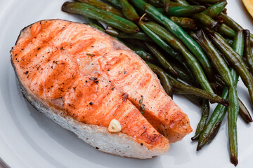 grilled salmon steak with string beans and lemon in a round white plate on a white background