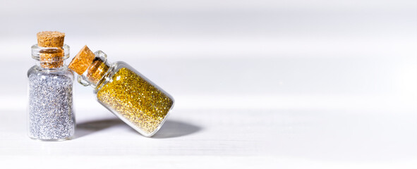Small Glass jars with golden and silver glitters for nail art and makeup on white background, Copyspace, Banner