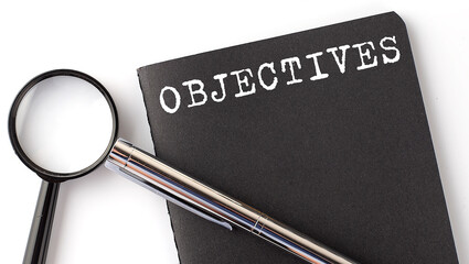 OBJECTIVES - business concept, magnifier with white text message on black notebook