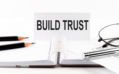 Text BUILD TRUST on paper card,pen, pencils, glasses,financial documentation on table - business concept