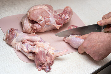 Cutting fresh chicken into pieces with a kitchen knife.