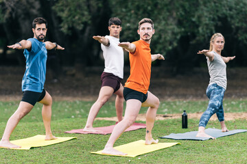 People raising arms while doing a yoga pose in a public park