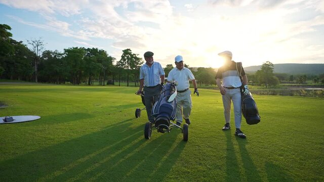4K Group of Asian people businessman and senior CEO enjoy outdoor sport  golfing together at country club. Healthy men golfer holding golf bag walking on fairway with talking together at summer sunset