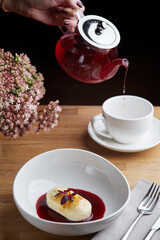 cheesecake with berry sauce and pouring red tea on background. breakfast morning table with flowers. cottage cheese pancakes.