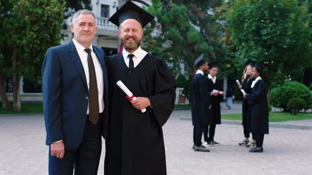 Emotional Day For Father And Son On The Graduation They Posing Together In Front Of The Camera While Holding Diploma