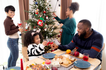 Happy African family eating food in dinner on festive thanksgiving eve day together at home, father and mother and children celebration party while decorating in xmas and new year in holiday.