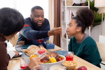 Obraz na płótnie Canvas Happy African family father feeding food with daughter in dinner on festive thanksgiving eve day together at home, father and mother and children celebration party in xmas and new year in holiday.