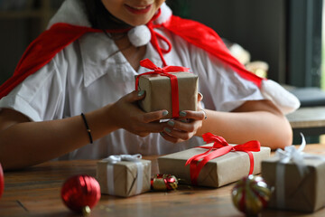 Cropped image of a beautiful woman holding a Christmas present box at the wooden table in the comfortable living room.