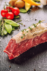 Raw beef steak fillet with ingredients like sea salt, pepper, onion and herbs on black board, product image for restaurant