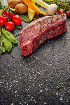 Raw beef steak fillet with ingredients like sea salt, pepper, onion and herbs on black board, product image for restaurant