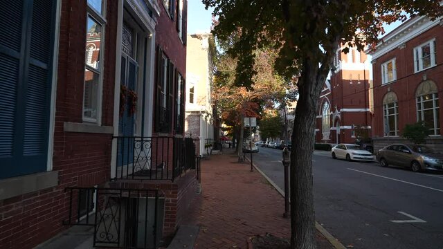 Frederick, MD, USA - 11 10 2021: An afternoon view of street in Frederick Maryland. Old historic town with vintage buildings on both sides. Autumn trees with colorful foliage.