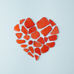 Broken glass pieces forming a red heart on a pastel blue background. Heartache minimal concept