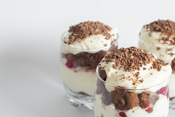 Biscuit cake with cream and cherries in a glass on a white background