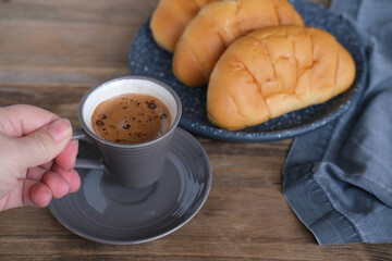 Cappuccino coffee in gray cup and saucer on an old wooden table, ruddy fresh croissants, concept fresh pastries, morning coffee, caffeine addiction, energy boost
