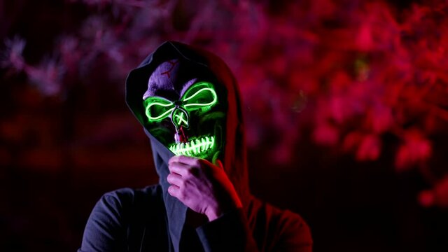 enigmatic figure of person with skull mask on face and hood on head, glowing in darkness