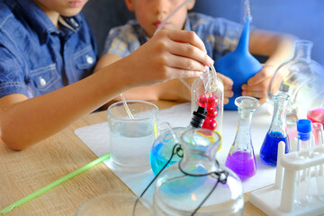Fototapeta premium two children 7-9 years old, elementary school boys, do chemical experiments, pour colored liquids into glass flasks, mix colors, school education concept, hands-on study of chemistry