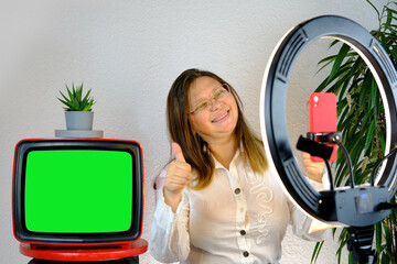 woman 40-45 years old, pretty female blogger sits in front of ring light and red smartphone,...