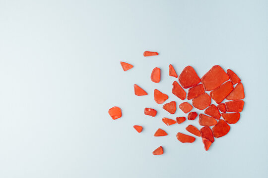 Shattered heart made of red glass pieces on a light blue background. Love minimal concept