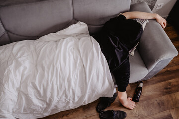 man lying on a couch with a headache or a hangover with a bottle of beer and a white blanket