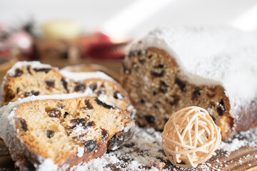Fototapeta premium Traditional Christmas stollen made of dried fruits and nuts sprinkled with powdered sugar on the background of a Christmas decor with candles. Traditional Christmas cupcake