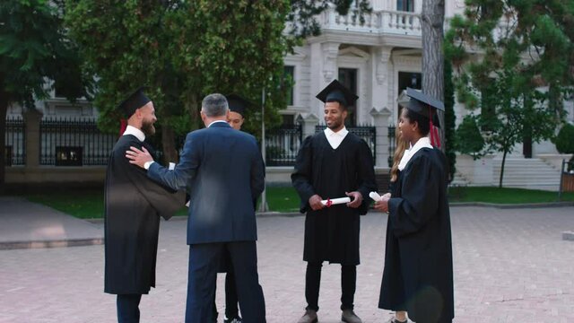 Charismatic principal of the college walking to his students multiracial and congratulated them after the end of graduation in the college park