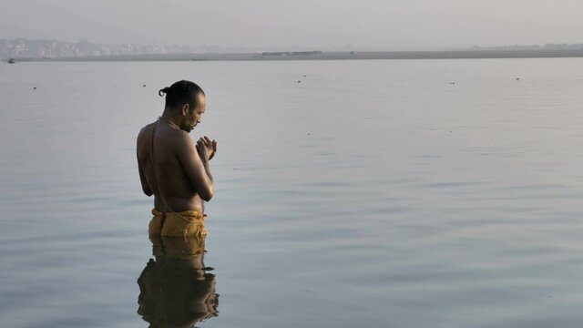 A Hindu priest or pandit standing in the water on the banks of the Ganges, bowing before the Sun in the morning and offering Suryanamaskar, and praying to the morning sun on the banks of  Varanasi.