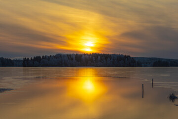 Wonderful winter sunset in Finland. Light is reflected from the water. The lake is almost frozen.