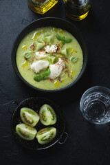 Bowl of green tomato gazpacho served with mozzarella, top view over black stone background, vertical shot