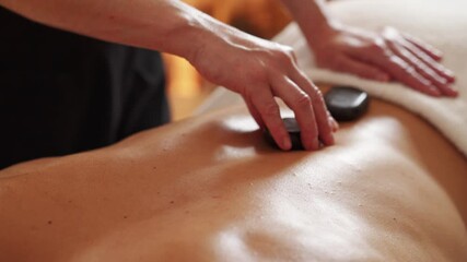 Hot stones massage. Close-up of masseuse placing hot stones on young man's back