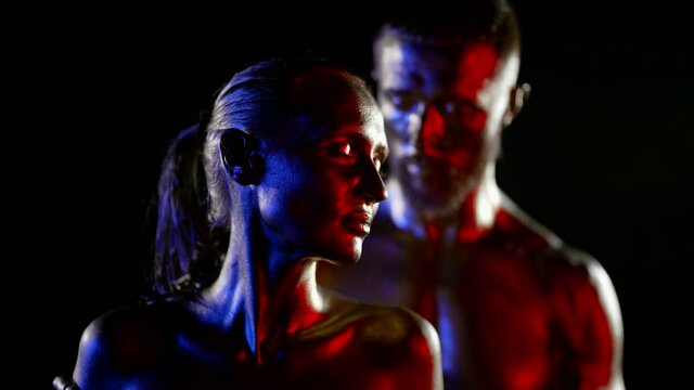 man and woman in golden dye, posing sensually in darkness, boyfriend is grabbing neck of girlfriend