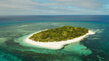 Tropical island and sandy beach surrounded by atoll and coral reef with turquoise water, aerial...