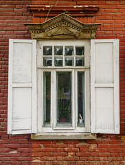 A carved wooden window with shutters on the facade of an old brick building. The picture was taken in Russia, in the city of Orenburg