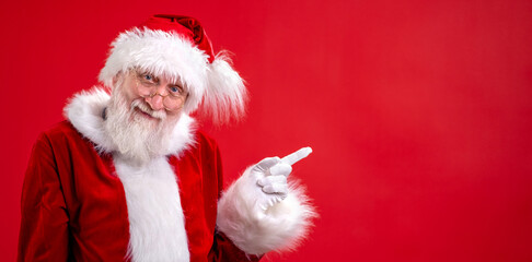 Banner Santa Claus pointing aside empty copy space on finger and looking showing blank place for advertised product or text on red studio background. Sale, Discount, Black Friday. Look at this