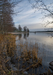 Pale Winter solstice reflex in the calm lake M&auml;laren, jump tower and icy reeds in the district Bromma in Stockholm