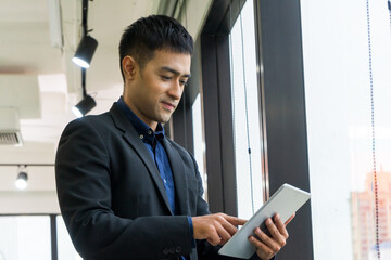 Young businessman executive in suit and smiling using tablet on window with city building background.