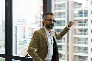 Fototapeta premium Bearded businessman executive in suit looking at camera on window with city building background.