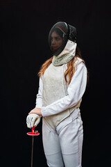 Portrait of a young fencer wearing white fencing costume and mask and holding the sword in front of...