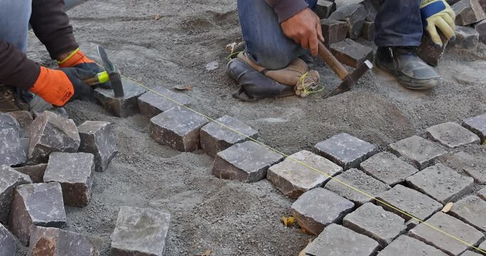 Industrial worker working paving using hammer pavement with granite stones cobblestones for paving road