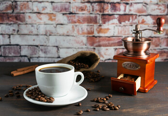Black coffee with cinnamon in a white cup on a dark wooden table. Roasted coffee beans on a saucer...