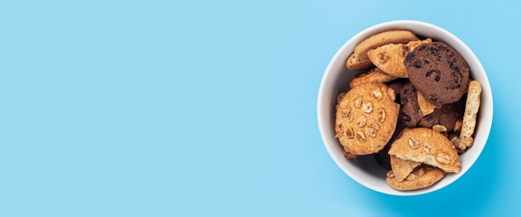 Cookies in a white bowl on a blue background. Top view, flat lay. Banner.