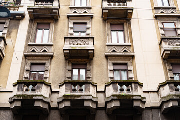 Facade of an old house with carved stone balconies and shutters on the windows. Milan, Italy