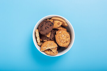 Cookies in a white bowl on a blue background. Top view, flat lay.
