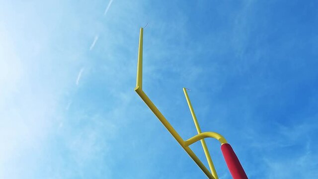 Looking up at yellow football goal post against the sky as a field goal is made during an American football game as the camera pans.