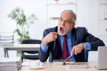 Old male employee having breakfast in the office