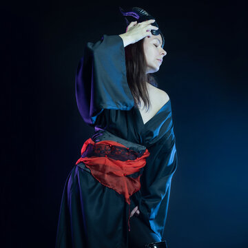 A demoness with horns and in a black kimono with a red belt, a costume of a mystical creature, a young woman in a fantasy gothic image, a portrait on black