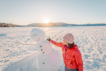 Woman making snowman in winter lake snow nature landscape having fun enjoying active winter...